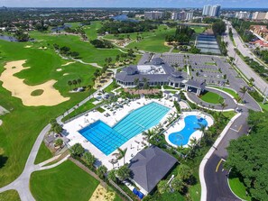 An aerial view of a golf course with a large swimming pool, a clubhouse, and surrounding greenery.