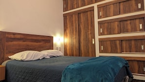 A bedroom with a wooden headboard, a bed with a quilted bedspread, and a built-in wardrobe with multiple compartments. - Moderna, Cómoda Suite Nube en Tepotzotlán centro (Tepotzotlán)