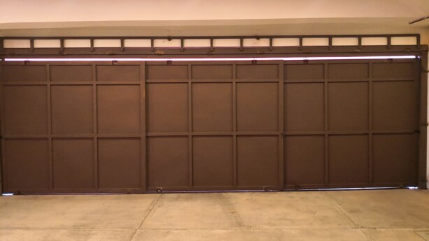 Een garage met een bruine schuifdeur, een betonnen vloer en een plafond met inbouwspots.