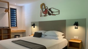 A bedroom with a bed, bedside tables, a wall-mounted artwork, and a window with blinds. - Villa Lune de Miel "champagne" Deshaies (Deshaies)
