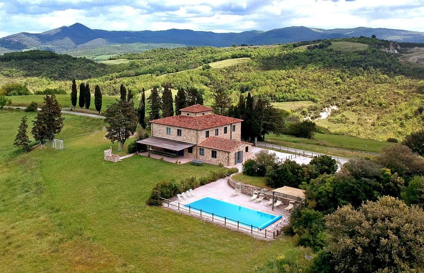 Une maison en pierre avec une piscine, entourée d’une végétation luxuriante et de collines.