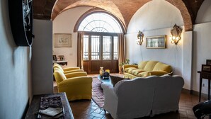 A living room with a high arched ceiling, a large window, and a yellow sofa. - Villa Elara - Tuscan Countryside Villa withPool (Montaione)