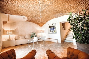 Ein großzügiger Wohnbereich mit hoher, strukturierter Decke, einem weißen Sofa, einem Couchtisch und einer Treppe, die zu einer weiteren Ebene führt.