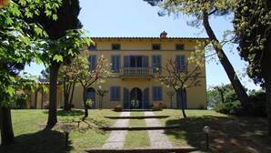 A yellow building with a central entrance, surrounded by a well-maintained garden with a stone pathway leading to the entrance. - Villa Elettra - Private villa with pool in Umbria (Castiglione del Lago)