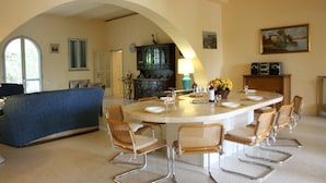 A dining area with a round table, wicker chairs, a blue sofa, and a kitchen in the background. - Villa Elettra - Private villa with pool in Umbria (Castiglione del Lago)