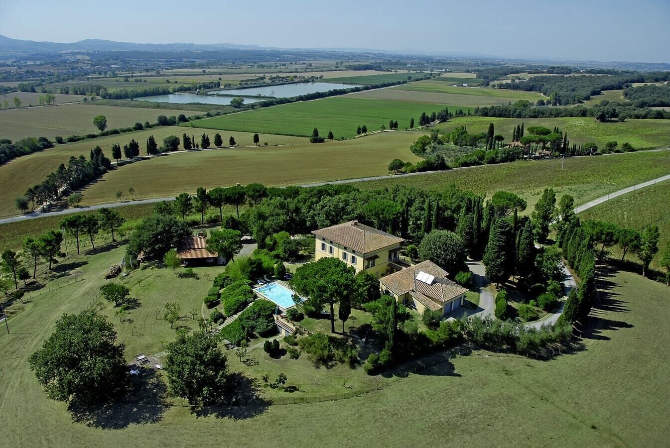 Vista aérea de una propiedad campestre con una casa grande rodeada de exuberante vegetación, una piscina y extensos campos.