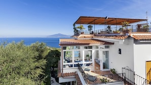 A coastal property with a terrace, a view of the sea, and a mountain in the distance.