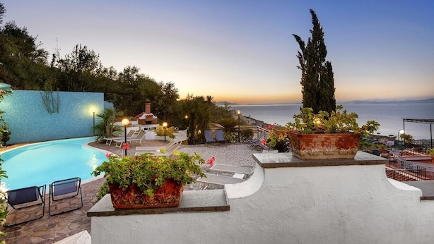 A poolside area with lounge chairs, a barbecue, and potted plants.