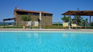 En bygning i sten med swimmingpool, liggestole og pergola.