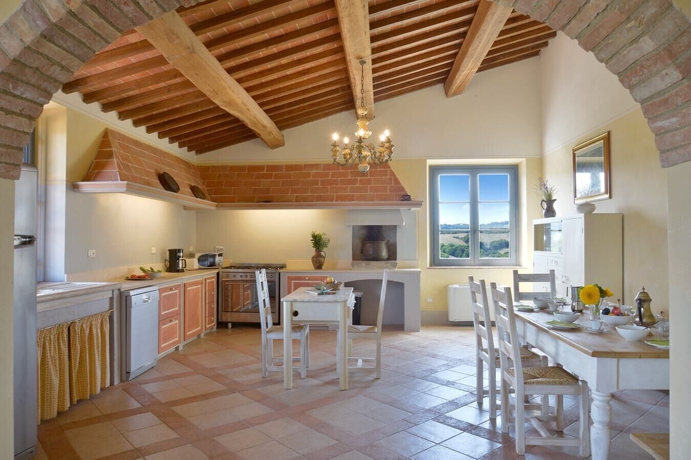 A kitchen with a brick fireplace, wooden ceiling beams, and a dining area with a table and chairs.