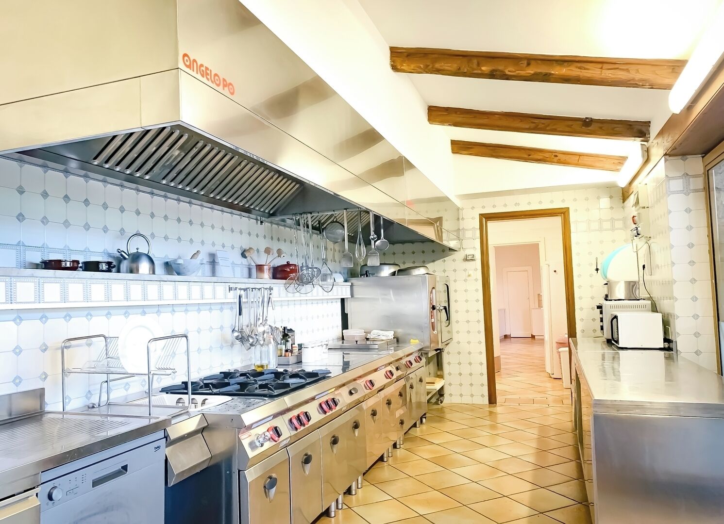 Une cuisine professionnelle équipée d’appareils en acier inoxydable, d’un pare-feu en carreaux et d’un plafond en bois.