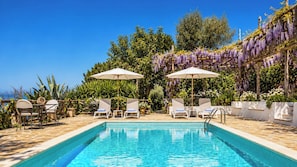 A poolside area with lounge chairs and umbrellas, surrounded by lush greenery and purple flowers. - Villa Donatella, Ideal For Large Groups (Massa Lubrense)