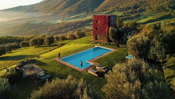 Un espace piscine doté d’une piscine rectangulaire, entourée d’une pelouse verdoyante et d’un bâtiment rouge.