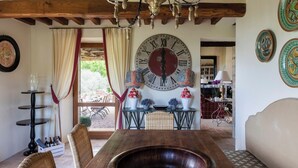Un coin repas avec une table en bois, des chaises, une grande horloge murale et un lustre.