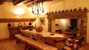 Een traditionele eetzaal met een lange houten tafel, banken en een stenen open haard.