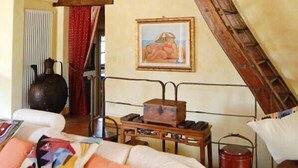Een rustieke kamer met een hoogslaper, houten balken, een klein tafeltje met een waterkoker en een schilderij aan de muur.
