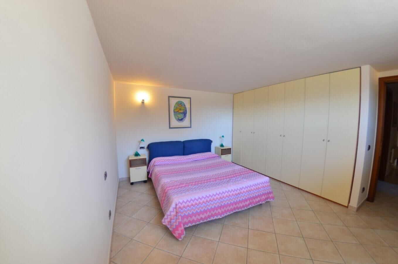 A bedroom with a bed, nightstands, a wardrobe, and a wall-mounted lamp.