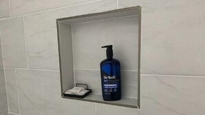 A bathroom with a white tiled wall and a small shelf holding a bottle of Dr. Teats Performance and a small tissue box. - 1BR 1B Hotel Like Ground Floor (Greenville)