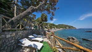 Une terrasse en bord de mer avec des murs en pierre, des rampes en bois et des chaises longues blanches.
