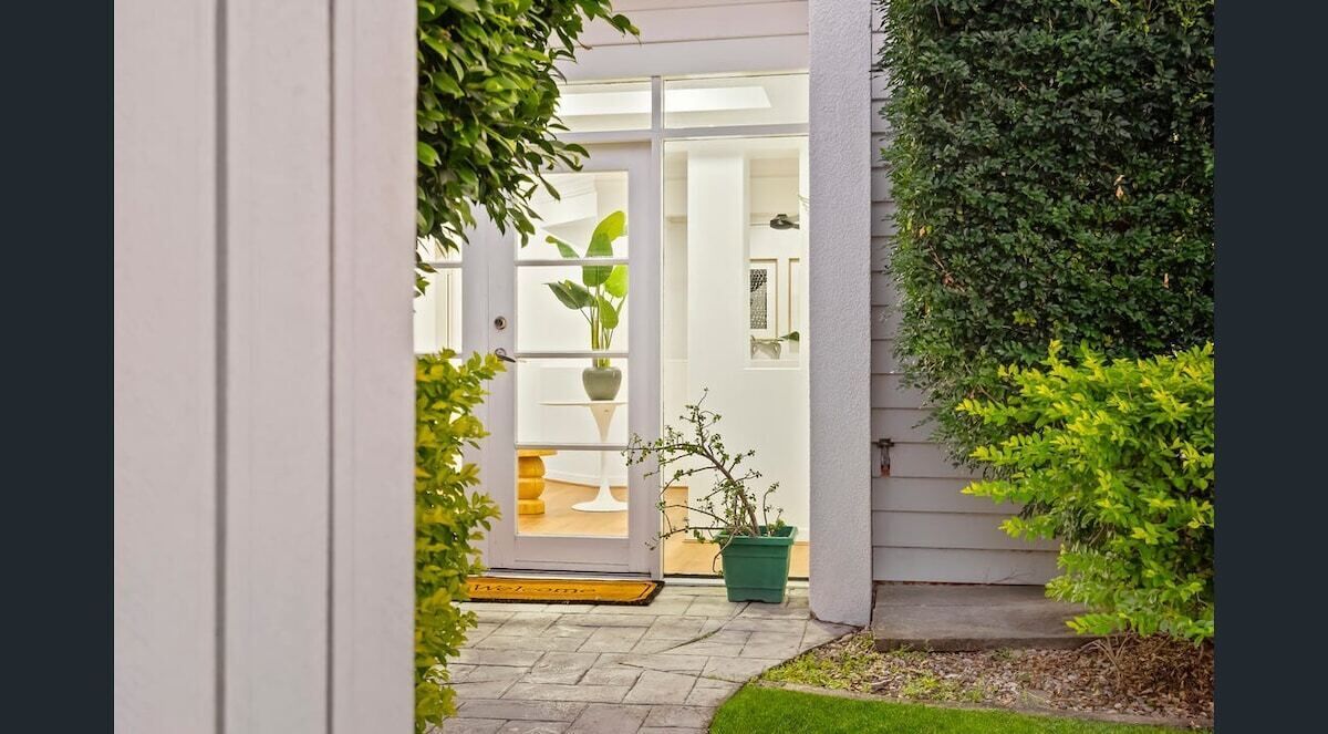 Une entrée de maison avec une porte blanche, un pot de fleurs et un petit jardin.