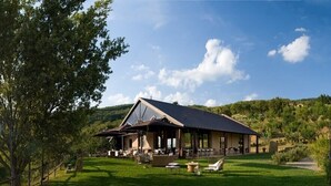 Uma casa com telhado inclinado, área de estar ao ar livre e vista para um campo verde e colinas ao fundo.