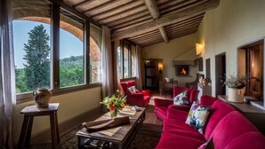 Uma sala de estar aconchegante com um sofá vermelho, uma mesa de centro de madeira e uma lareira. Janelas amplas oferecem vista para o exterior.
