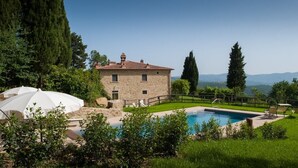 Uma casa de pedra com piscina, rodeada por vegetação e montanhas ao fundo.
