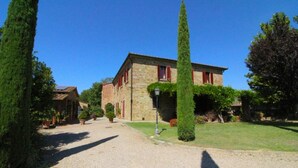 A stone building with red shutters, a gravel driveway, and neatly trimmed hedges. - Villa Fausta - Tuscan Countryside Villa with Pool (Castiglion Fiorentino)