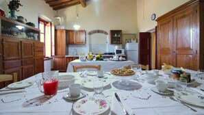 A dining area with a table set for four, a kitchen in the background, wooden cabinets, and a rustic ceiling. - Villa Fausta - Tuscan Countryside Villa with Pool (Castiglion Fiorentino)