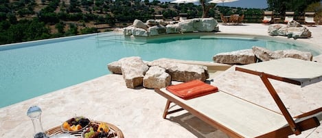 A poolside area with lounge chairs, a table with a fruit basket, and a view of the surrounding landscape.