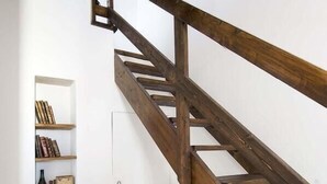 Una escalera de madera con un banco y un estante con libros y botellas.