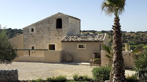 Un edificio de piedra con tejado de baldosas, una estructura pequeña adosada y un patio de grava.