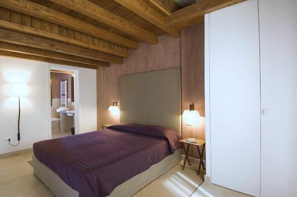 A bedroom with a large bed, wooden ceiling beams, and two bedside lamps.