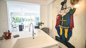 A modern kitchen with a large white sink, a dining area with a glass table and chairs, and a mural on the wall.