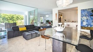 A modern living room with a glass dining table, grey sofa, and a unique white sculpture.