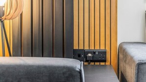 Een moderne kamer met een wand van verticale houten panelen, een bureau met lamp en twee grijze banken.