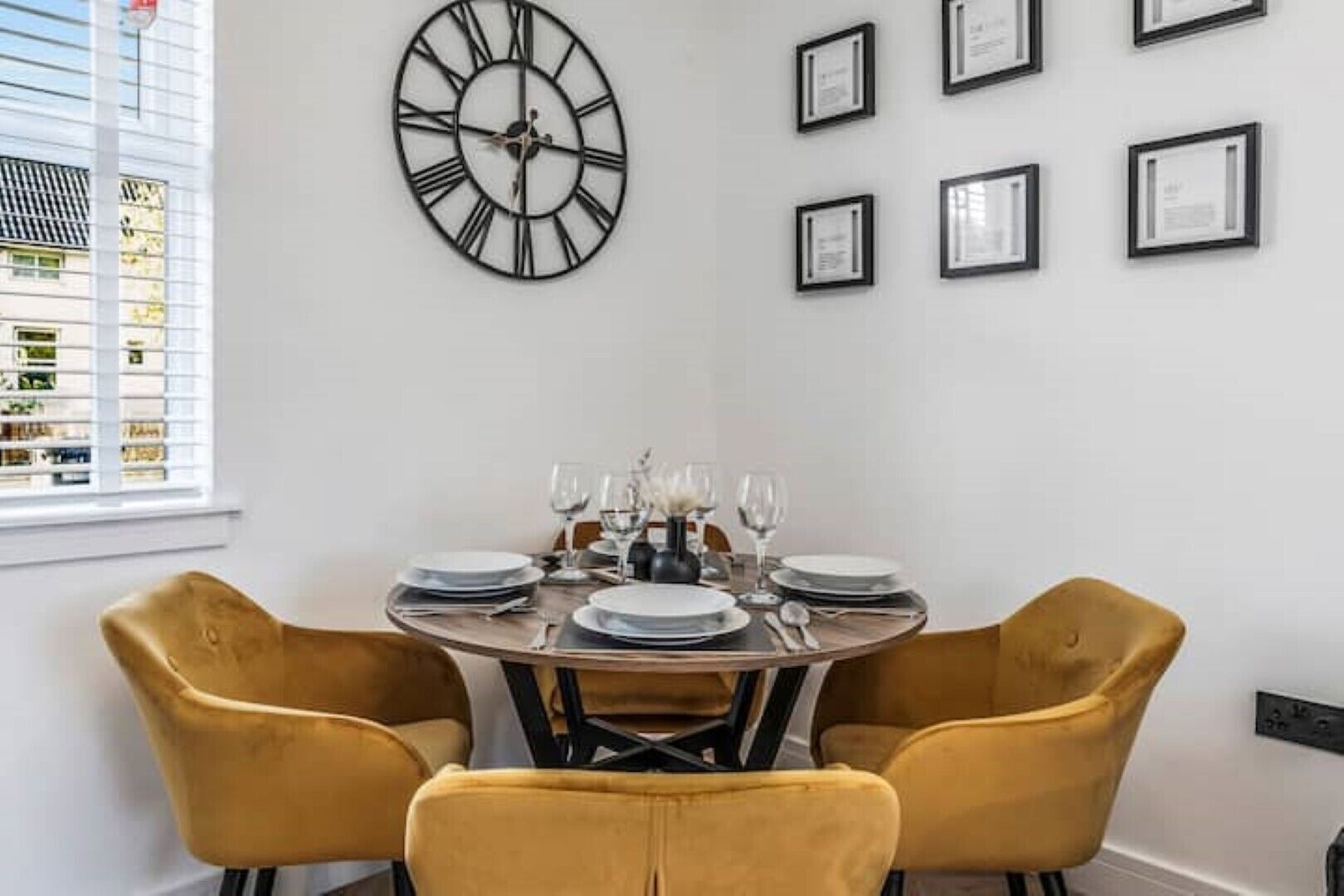 A dining area with a round table set for four, yellow chairs, and a large wall clock.