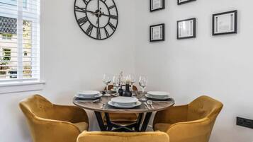 A dining area with a round table set for four, yellow chairs, and a large wall clock.