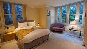 A bedroom with a bed, a nightstand, a chair, and large windows. - Stunning & Modern 2BD Flat - Manchester! (Salford)