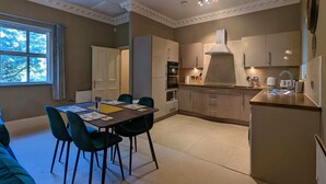 A compact kitchen with modern appliances, a dining area with a table and chairs, and a view of the outdoors through a window. - Stunning & Modern 2BD Flat - Manchester! (Salford)