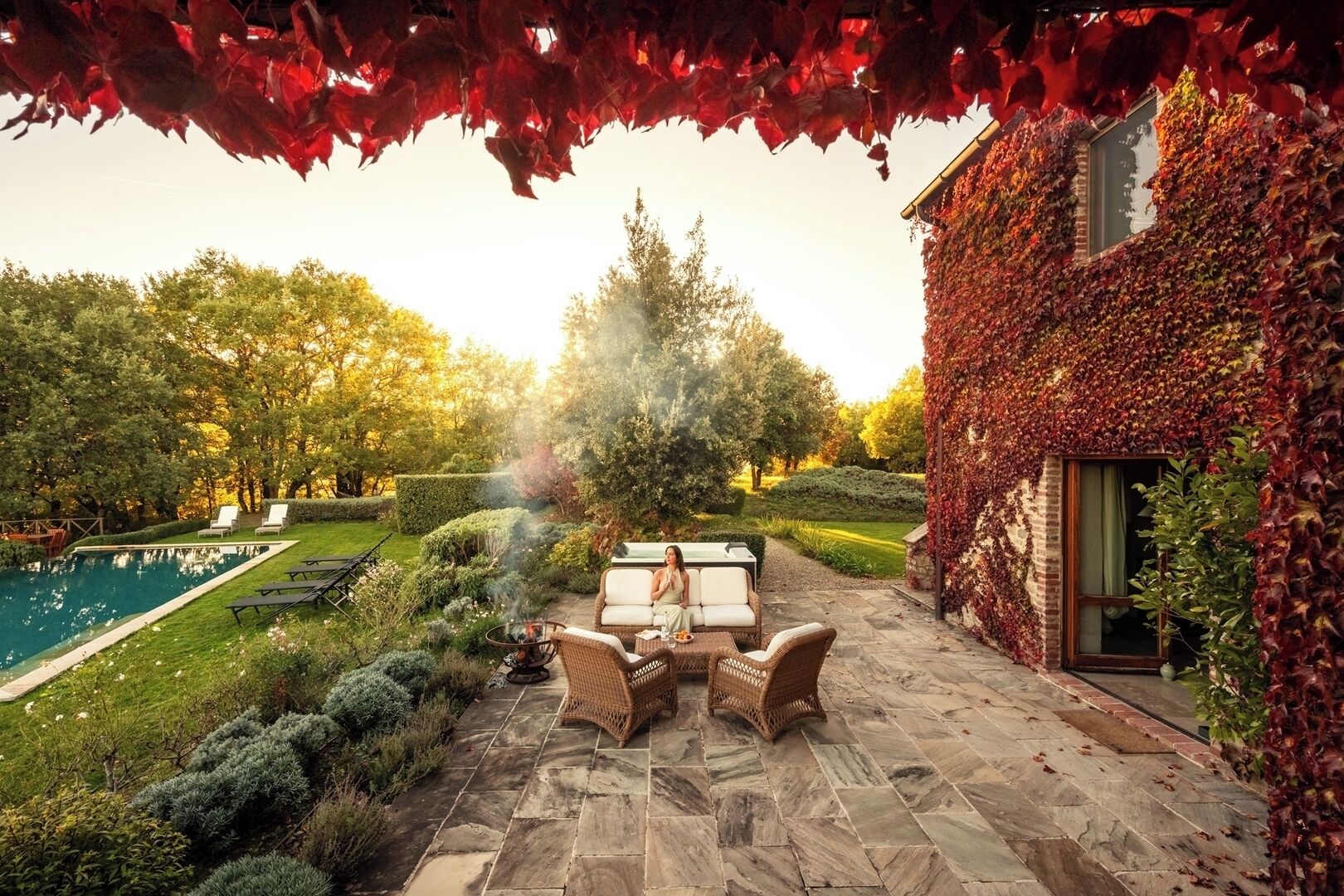 Une terrasse avec un foyer, des meubles en osier et une piscine.