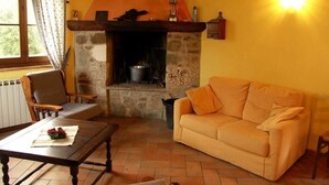 Uma sala de estar acolhedora com lareira de pedra, um sofá, uma mesa de centro de madeira e uma janela com cortinas.