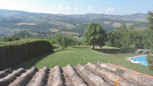 A view from a balcony overlooking a landscaped garden with a swimming pool and distant hills.