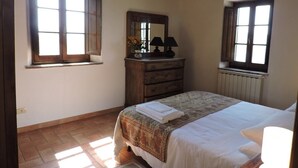 A bedroom with a bed, dresser, mirror, and two windows.