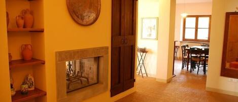 A room with a fireplace, wooden shelves, and a dining area with chairs and a table.