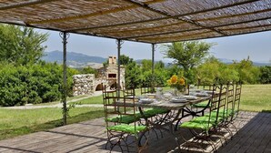 An outdoor dining area with a stone oven, green cushioned chairs, and a table set for four. - Villa Bibbona - Private villa with heated pool (Montecatini Val di Cecina)