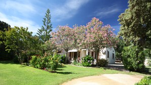 Une maison avec une allée pavée, entourée de pelouses bien entretenues et d’arbustes en fleurs.