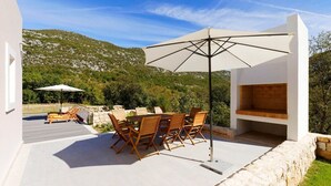 Une terrasse extérieure avec une table et des chaises, un grand parasol et une cheminée en pierre.