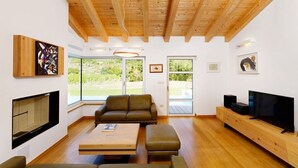 Un salon moderne avec un plafond en bois, un canapé, une table basse, un téléviseur et des œuvres d’art accrochées aux murs.