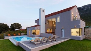 Une maison moderne à deux étages, dotée d’une piscine, d’un espace de détente extérieur et d’un mur en pierre.